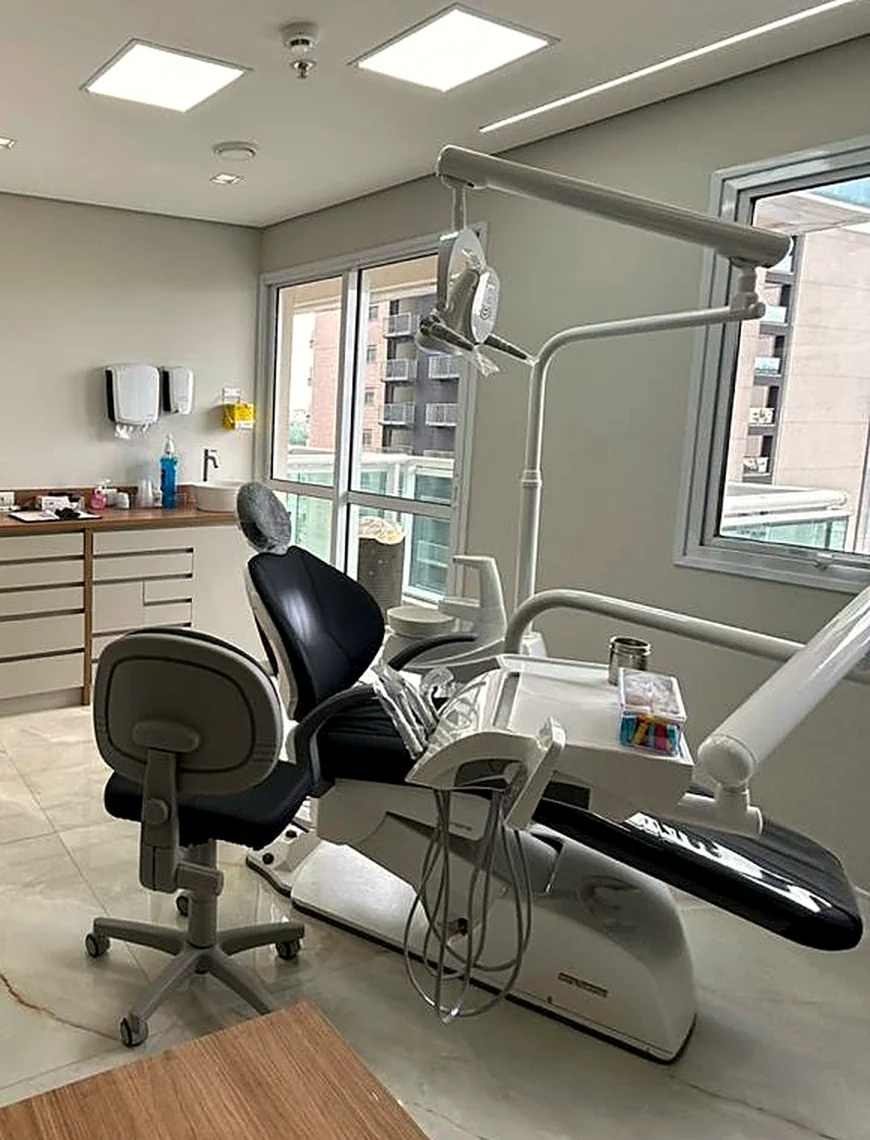Estação clínica da Lily Asher: cadeira odontológica, refletor e bancada, com luz natural da janela